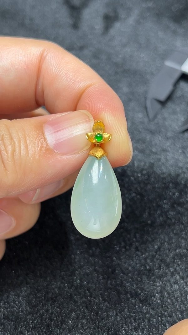 這款天然A級翡翠18K金鑲嵌水滴吊墜（編號#299），採用色澤清新柔和的淺綠色翡翠精工雕琢，水滴造型線條圓潤流暢，如露珠凝翠、靜靜垂掛胸前，展現自然與靈動之美。翡翠質地通透溫潤，飽含東方玉石的靈性與氣韻；外圈採用18K金鑲嵌設計，細膩包邊，不僅提升整體質感，更增添了一抹現代奢雅氣息。此款設計極具女性柔美氣質，是日常佩戴或優雅禮贈的上乘之選。